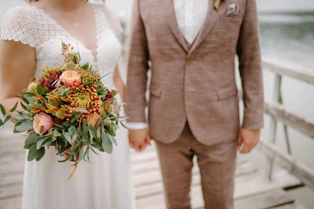 Hochzeitspaar steht am Steg am Schliersee im Herbst in Nahaufnahme