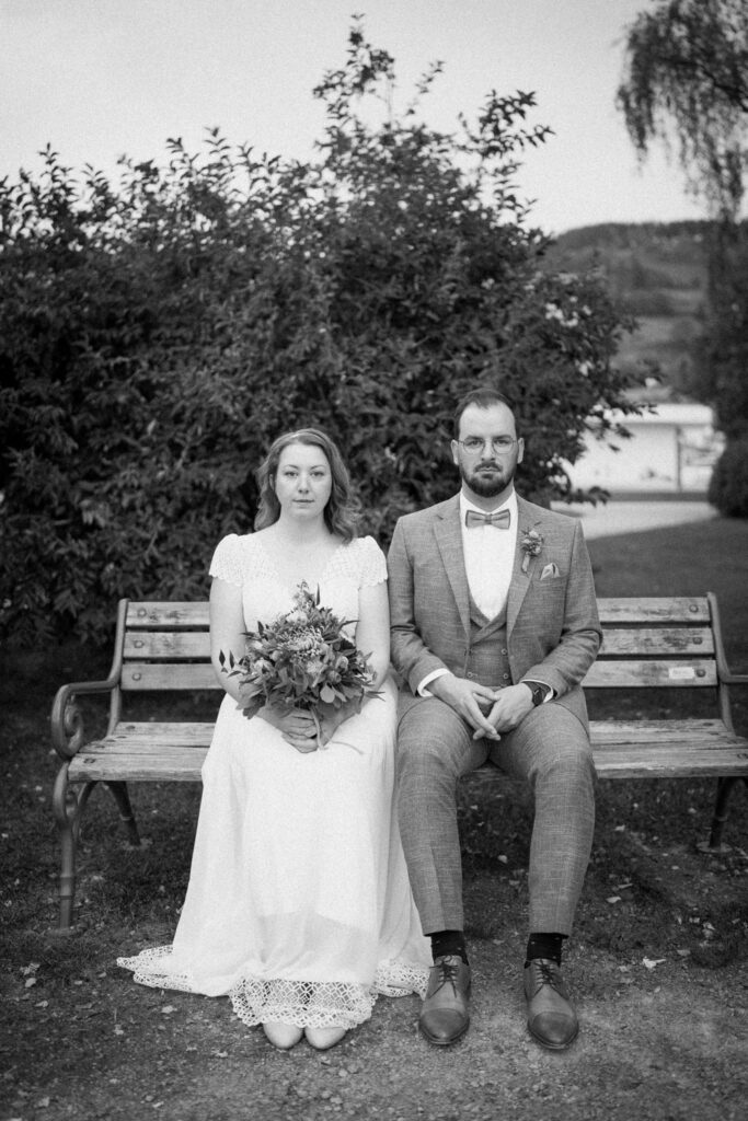 Hochzeitspaar sitzt auf Bank am Schliersee vor ihrer Hochzeit in Schliersee Rathaus